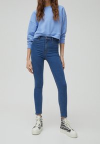 Modrý zkrácený svetr a skinny jeans se zvýšeným pasem ve středně modré džínovině. Boty jsou bílé s černým zebra vzorem.