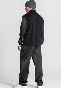 Černý fleecový a saténový sportovní komplet s vysokým límcem a elastickými manžetami, doplněný o šedou pletenou čepici a bílé tenisky.