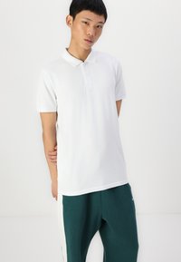 Vit polotröja med korta ärmar, krage och tre knappar. Kombinerad med gröna sweatpants med en sidouppskrift.