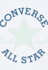 Tejido blanco con una gran estrella verde y texto en azul oscuro que dice "CONVERSE" en la parte superior y "ALL STAR" en la parte inferior, con "Chuck Taylor" debajo.