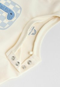 Crèmekleurig baby rompertje met een blauw gestructureerd nummerdesign, drukknoopjes aan de onderkant en gemaakt van zachte katoen.