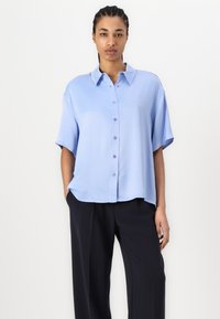 Light blue short-sleeve button-up shirt with a collar, smooth texture, and relaxed fit; worn with dark navy pants.