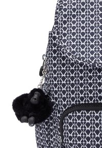 Sac à dos bleu marine avec motif géométrique blanc, doté d'une poche zippée à l'avant et d'un porte-clés peluche gorille noir attaché par une chaîne argentée.
