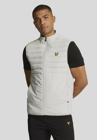 gilet rembourré blanc avec texture matelassée verticale, fermeture éclair frontale et poches latérales. Présente un petit logo jaune sur le côté gauche de la poitrine.
