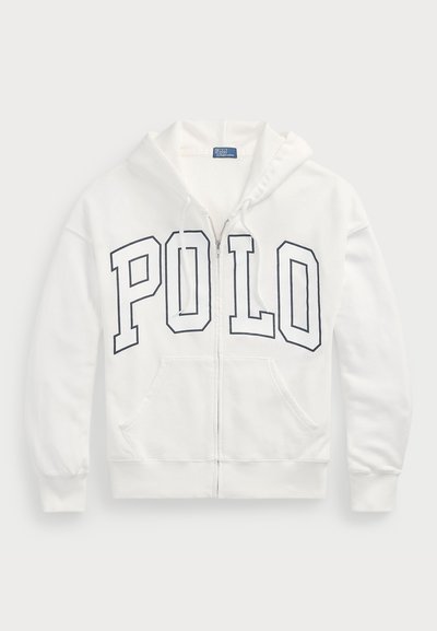 Bela zip-up kapuca iz mehkega materiala, z velikim mornarsko modrim grafičnim napisom "POLO" spredaj. Ima dva sprednja žepa in kapuco s vezalko.