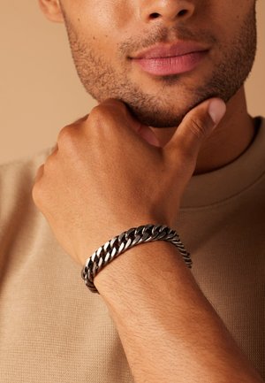 Silver chain bracelet on a wrist, featuring interlocking links with a polished finish. Skin tone is medium, with a subtle, smooth texture.