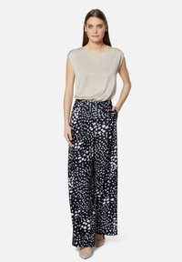 Light beige, smooth blouse with short sleeves; black wide-leg trousers featuring a white and pale blue splatter pattern, with pockets.