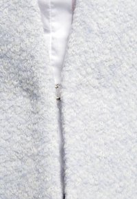 Cappotto blu chiaro con una texture morbida e pelosa. Presenta una cerniera argentata sul davanti e un rivestimento interno liscio.