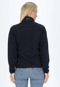 Marintröja i fleece med hög krage, dragkedja och subtila detaljer bak. Kombinerad med åtsittande blå jeans. Mjuk, texturerad väv.