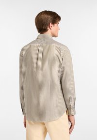Camicia a righe beige e bianca, con colletto a punta, polsini abbottonati e una piega sulla schiena per facilitare i movimenti. Tessuto liscio e leggero.