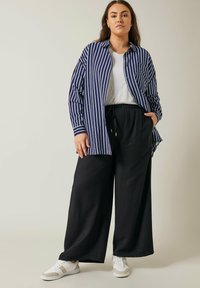 Camisa de raya oversized en azul marino y blanco con botón en la parte delantera, combinada con pantalones de pierna ancha negros y zapatillas blancas, con un ajuste relajado.
