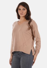 Maglione beige a maniche lunghe con scollo a V, dal taglio morbido e con spacchi laterali, caratterizzato da una texture liscia e cuciture minime.