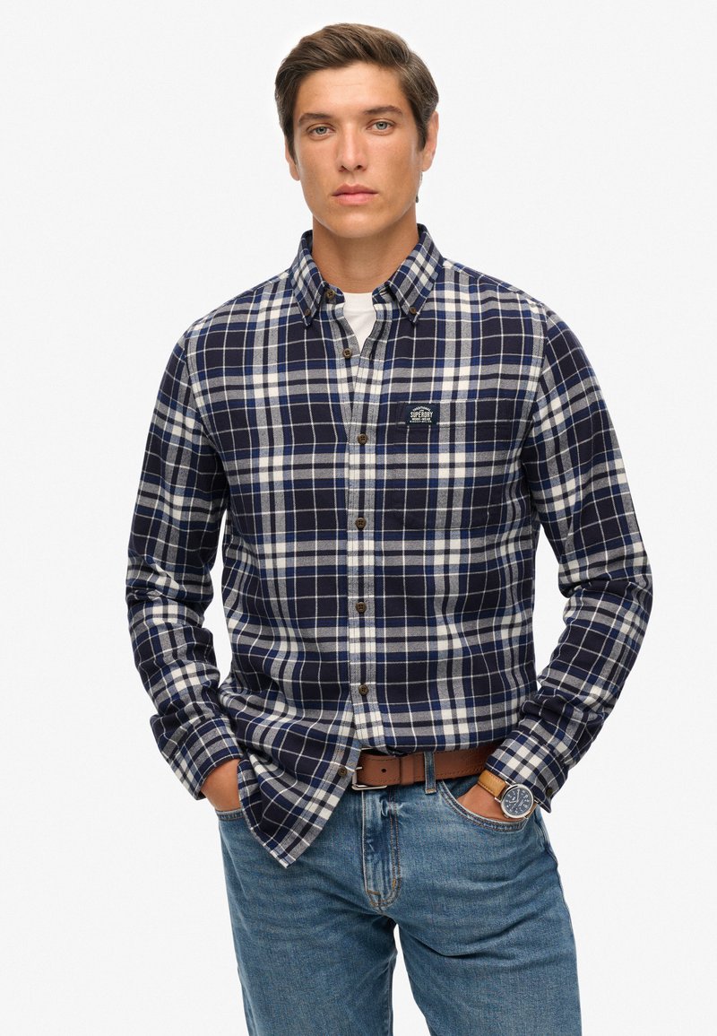 Geruit overhemd met lange mouwen in marineblauw, wit en grijs. Voorzien van een button-down kraag, borstlogo en een losse pasvorm. Draagt bij blauwe spijkerbroek.