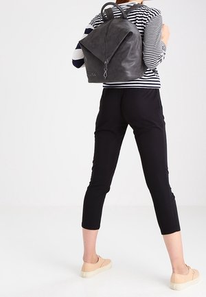 Person wearing black cropped pants, beige sneakers, striped long-sleeve top, carrying a dark gray leather backpack on their back.