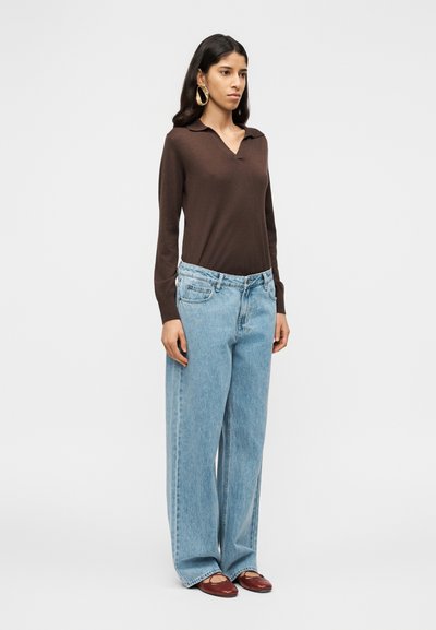 Καφέ πουκάμισο πόλο με μακριά μανίκια, μπλε τζιν παντελόνι με φαρδιά μπατζάκια, μπορντό παπούτσια και μεγάλα χρυσά κρίκοι σκουλαρίκια. Απλός σχεδιασμός, λεία υφή.