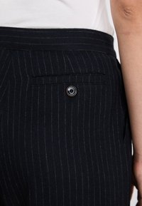 Pantaloni navy a righe sottili con una cintura larga e una tasca posteriore con un dettaglio in metallo a forma circolare, realizzati in un tessuto testurizzato.