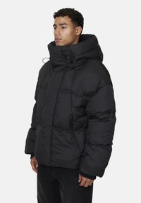Giacca a vento nera con colletto alto, dalla vestibilità oversize e polsini elasticizzati. Presenta tasche con zip e una texture liscia e lucida.