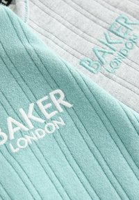 Dzianina o fakturze w kolorze miętowym i jasnoszarym, z haftem "BAKER LONDON". Żebrowany wzór dodaje szczegółów i głębi.