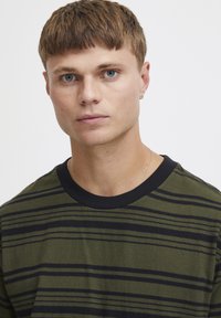Camiseta verde oliva con rayas horizontales negras, mangas cortas, cuello redondo de canalé negro y una textura de algodón suave.