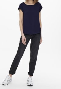 Top blu navy a maniche corte con scollatura rotonda, abbinato a jeans neri con risvolti e scarpe da ginnastica bianche con dettagli neri.