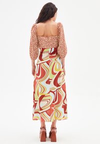 Robe longue avec des manches bouffantes, un haut à imprimé léopard, une jupe fluide aux motifs tourbillonnants multicolores et des sandales à talons blocs.
