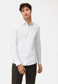Witte lange mouwen shirt van gladde stof, met een puntige kraag en knoopsluiting aan de voorkant. Aangesneden ontwerp met een subtiele glans.
