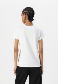 T-shirt en coton blanc à manches courtes, col ras du cou classique et coupe droite. Texture lisse, design minimaliste, sans motifs visibles.