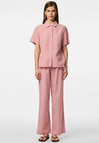 Camicia a righe rosse e bianche con maniche corte e colletto, abbinata a pantaloni larghi e dritti dello stesso colore. Sandali neri piatti.