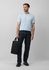 Hellblaues kurzärmeliges T-Shirt, dunkle Denim-Jeans und schwarze Tragetasche. Schwarze Schuhe mit glatter Oberfläche. Einfaches und lässiges Outfit.