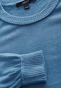 Světle modrý pletený svetr s vroubkovaným kulatým výstřihem a elastickými manžetami, který předvádí měkkou strukturu a rovnoměrný vzor stehů po celém povrchu.