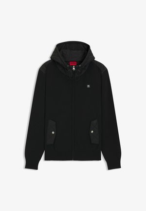 Felpa nera con zip frontale, spalle trapuntate e tasche. Presenta un cappuccio regolabile con coulisse e un piccolo logo sul petto.