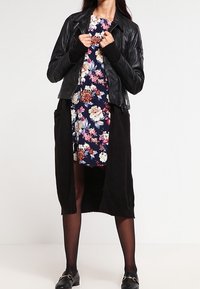 Černá kožená bunda přes květinové šaty s tmavým dlouhým kardiganem. Šaty mají vícebarevné květiny na tmavě modrém podkladu.