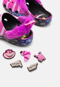 Roze Crocs met paarse bontaccenten, versierd met pootafdrukken en geanimeerde karakteraccessoires, waaronder pins en charms in verschillende kleuren.