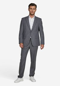 Costume gris à motifs avec une coupe ajustée, blazer à un bouton et deux poches avant, associé à une chemise blanche et des baskets blanches.