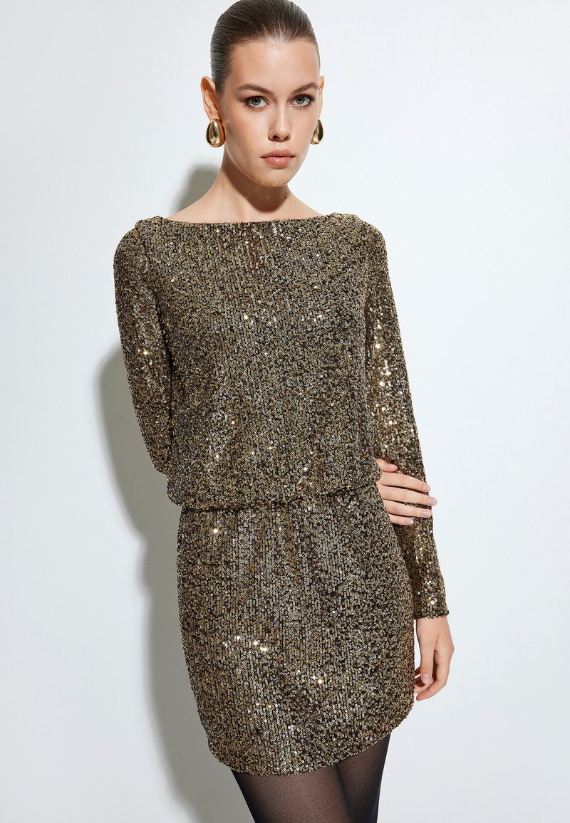 Robe en sequins dorés scintillants avec des manches longues, un col bateau et une taille froncée, réfléchissant la lumière grâce à une surface texturée.