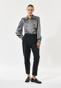 Graues satinierte Hemd mit Puffärmeln und Rüschensaum, kombiniert mit schwarzen maßgeschneiderten Hosen und schwarzen Slippern.