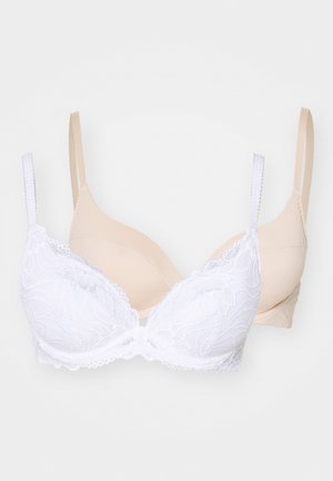 Biała koronkowa bielizna z kwiatowym wzorem i falbankami w zestawie z gładkim beżowym stanikiem. Oba mają regulowane ramiączka i wsparcie w postaci fiszbin.