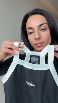 Μαύρο τοπ χωρίς μανίκια με λευκή επένδυση, με κεντημένο λογότυπο «adidas» στο μπροστινό μέρος. Το ύφασμα φαίνεται λείο· οι τιράντες είναι ρυθμιζόμενες και φαρδιές.