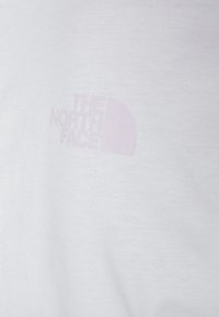Bílá tričko vyrobené z bavlny s jemnou texturou. Na levé straně hrudi se nachází světle růžové logo "The North Face".