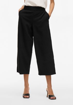 Pantalones cortos de pierna ancha en negro, confeccionados con una tela texturada, con una cinturilla elástica y bolsillos laterales, que cuentan con aberturas laterales para un toque adicional.