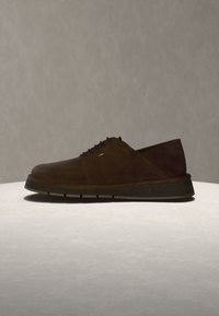 Ανδρικό σκούρο καφέ δερμάτινο παπούτσι με κορδόνια και χοντρή σόλα, εκτεθειμένο σε ανοιχτό γκρι επιφάνεια με απλό γκρι φόντο.