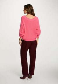 Maglione rosa lavorato a maglia con maniche larghe, abbinato a pantaloni attillati bordeaux e stivaletti con tacco bordeaux, mostrato da dietro.