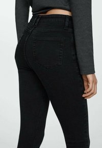 Jeans negros de talle alto con una forma ajustada, que cuentan con bolsillos traseros y una textura limpia y suave. La tela parece elástica y ajustada al cuerpo.