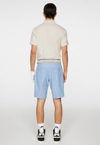 Ljusbeige polo skjorta tillsammans med ljusblå shorts. Outfiten har ett vävt beige bälte och en golfhandske på vänster hand.
