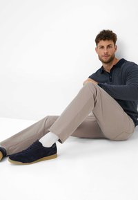 Polo shirt navy a trama, pantaloni slim-fit beige chiaro e sneakers in suede navy con suole in gomma, indossati con calzini bianchi a crew.