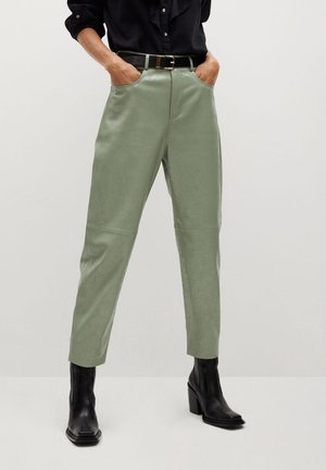 Groene neplederen broek met een hoge taille, zijzakken en een gladde afwerking, gecombineerd met zwarte blokhaklaarzen en een zwart shirt.