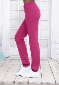 Fuchsia Jogginghosen mit entspannter Passform, elastischem Bund und gerippten Bündchen, kombiniert mit weißen Sneakers auf einem Holzboden.