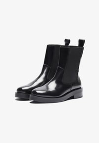 Bottines noires avec une finition brillante, des panneaux latéraux élastiques, des languettes de tirage et une semelle épaisse. Texture lisse et design minimaliste.