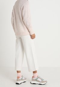 Person in einem hellrosa flauschigen Pullover, weißen weit geschnittenen, gekürzten Hosen, pastellrosa Socken und beigen, weißen und mintgrünen Sneakers, der seitlich steht.