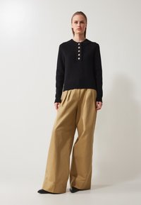 Svart ribbad tröja med knapplist och långa ärmar, i kombination med lösa beige byxor som har vida ben och en mjuk textur.